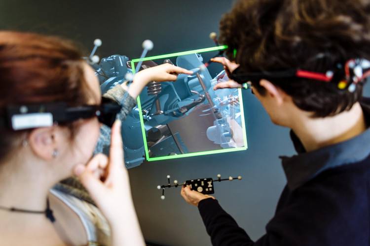 Zwei Personen sind von hinten zu sehen, tragen VR-Brillen und begutachten ein digitales Modell einer technischen Gerätschaft