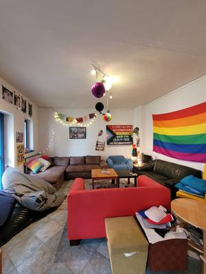 Auf dem Foto ist die Innenansicht des queeren Jugendzentrums zu sehen, eine große Regenbogenflagge sowie Sofas sind zu sehen.