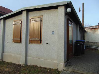 Auf dem Bild ist das Gebäude des Jugendzimmers Possendorf zu sehen. Die Fassade ist grau, die Tür und braune Fensterläden sind zu sehen.