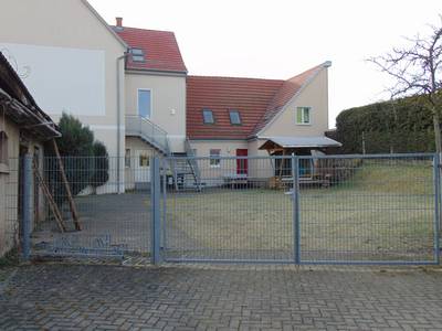 Das Bild zeigt die Außenfassade des Jugendzimmers, ein großes Tor sowie eine Holzsitzgruppe sind zu sehen,