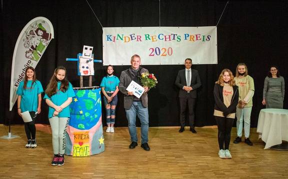 Die Kinderjury, der Oberbürgermeister Peter Kleine und die Kinder- und Jugendbeauftragte Sina Solaß übergeben den Kinderrechtspreis 2020 an Ulrich Dillmann von der Volkshochschule.
