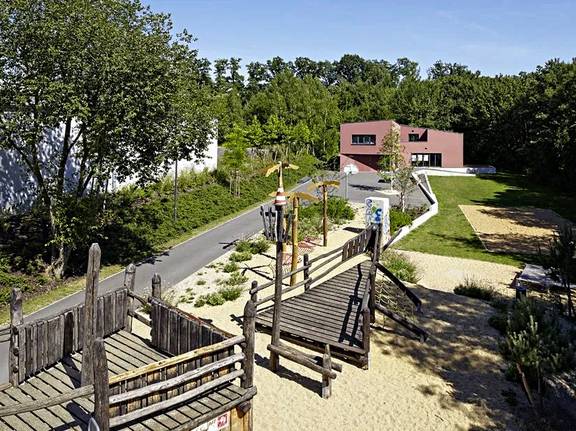 Auf dem Bild zu sehen ist das Außengelände des Jugendclubs Cafe Conti. Zu sehen ist der Spielplatz und die Fassade in rot.