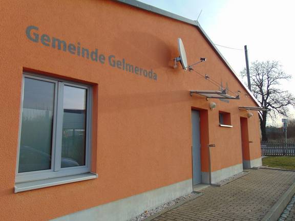 Das Bild zeigt die Außenfassade des Jugendzimmers Gelmeroda. Die Fassade ist orange und es ist der Schriftzug Gelmeroda sowie die Tür zu sehen.