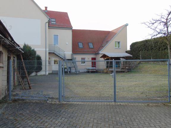 Das Bild zeigt die Außenfassade des Jugendzimmers, ein großes Tor sowie eine Holzsitzgruppe sind zu sehen,