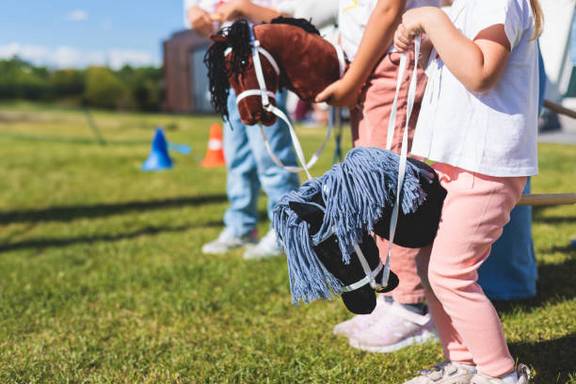 Auf dem Bild sind Kinder auf Steckenpferden auf einer Wiese zu sehen.