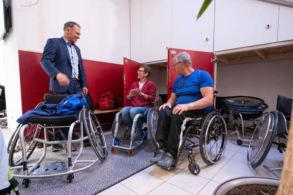 Ein Rollstuhlbasketballer und eine Rollstuhlbasketballerin mit Oberbürgermeister Peter Kleine vor den neuen Schränken