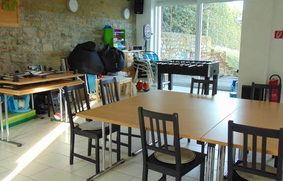 Auf dem Bild ist das Jugendzimmer Süßenborn von innen zu sehen, man blickt Richtung Terasse und sieht einen Tisch mit Stühlen.