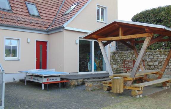 Auf dem Bild ist die Terasse mit Sitzgurppe und die rote Eingangstür des Jugendzimmers Süßenborn zu sehen.