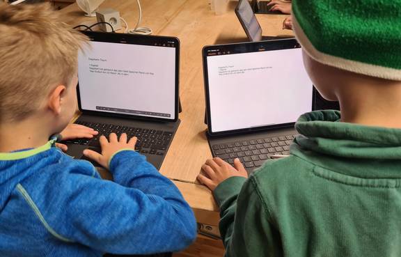 Auf dem Bild sind zwei schreibende Kinder am PC zu sehen.