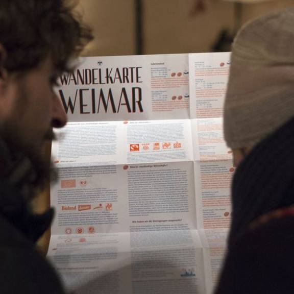 Zwei Interessierte schauen sich die Hintergrundinformationen auf der Rückseite der Weimarer „Wandelkarte“ an.