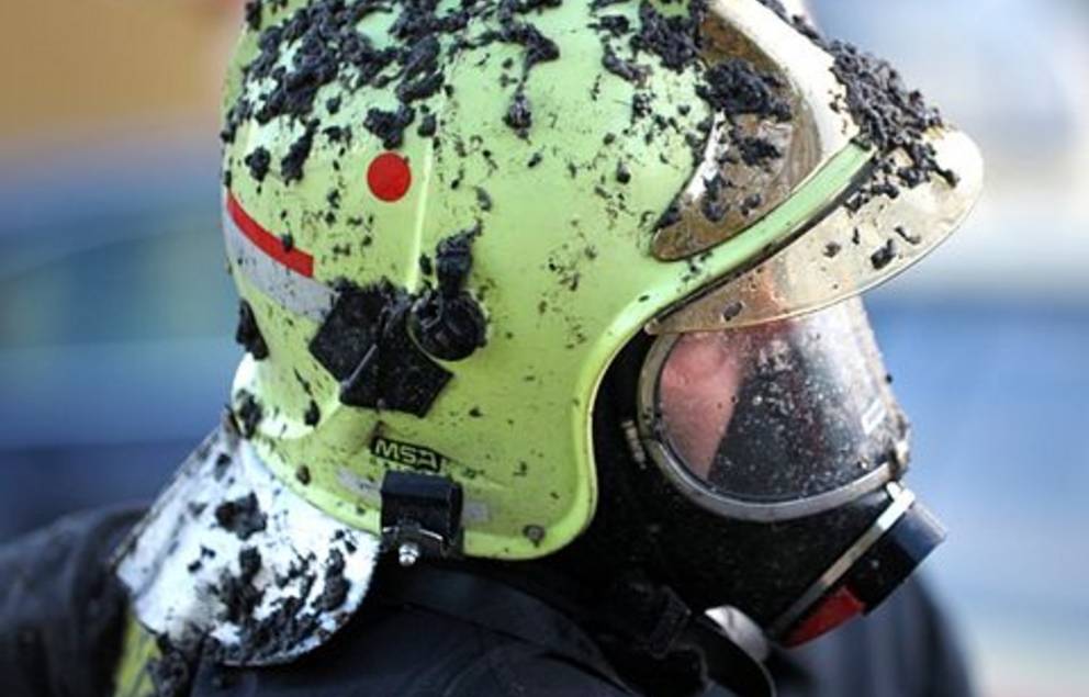 Person der Feuerwehr mit dreckigem Helm (Detailaufnahme Kopf)