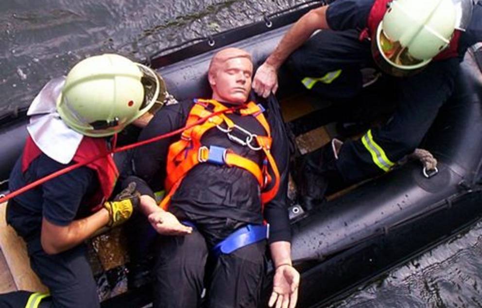 Zwei Feuerwehrleute in kompletter Montur in einem Schlauboot versorgen Opfer (Dummy). Aufnahme von oben.