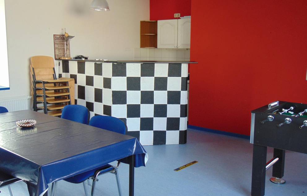 Auf dem Bild ist die Innenansicht des Jugendzimmers Tröbsdorf zu sehen, man sieht den Thresen und eine rote Wand.