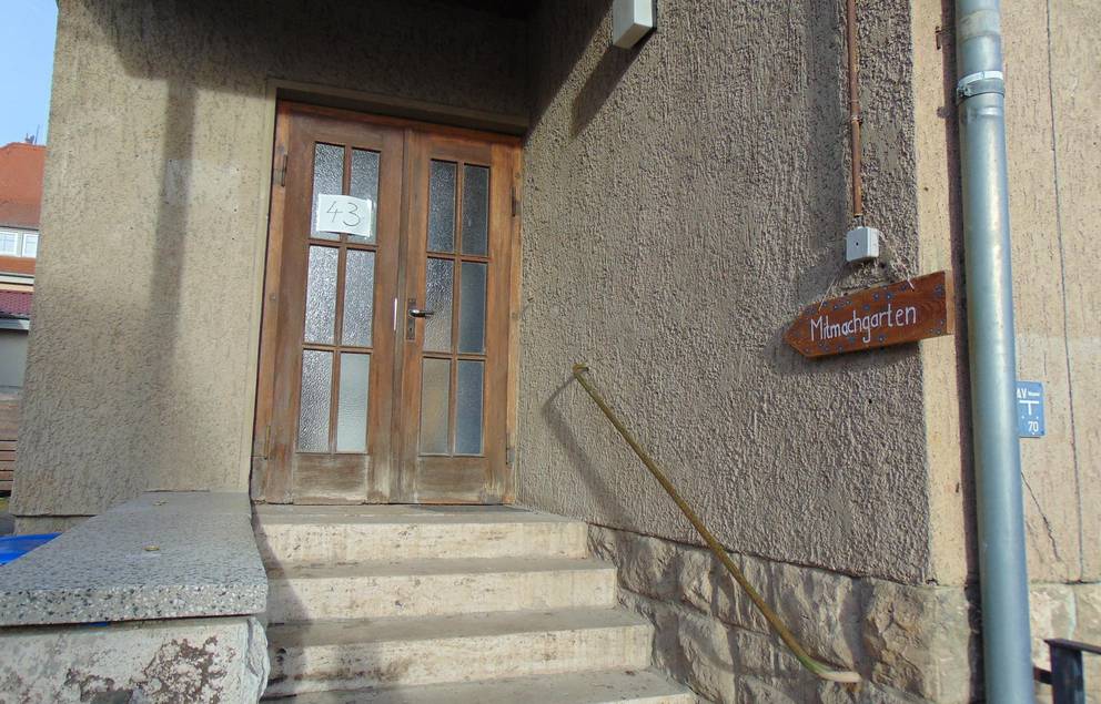 Auf dem Bild ist der Treppenaufgang zum Jugendzimmer Taubach zu sehen und das Schild mit der Aufschrift Mitmachgarten.