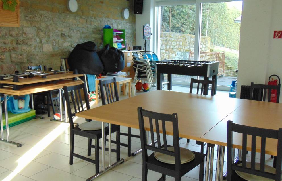 Auf dem Bild ist das Jugendzimmer Süßenborn von innen zu sehen, man blickt Richtung Terasse und sieht einen Tisch mit Stühlen.